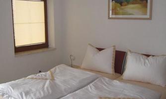A simple bedroom with a double bed and white bedcovers. An artwork hangs on the wall, and a window with blinds provides daylight.