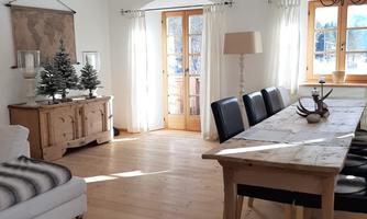 A bright and cozy dining room with a large wooden table and black chairs. The windows let in plenty of light and there is a beautiful decoration in the background.
