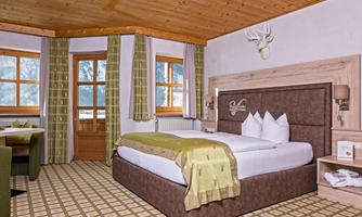 A cozy bedroom with a large bed and green curtains. Wooden ceiling and windows provide a view of nature.