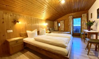 A cozy room with a wooden ceiling and two single beds. Large windows let in natural light, and there is a seating area with a view outside.