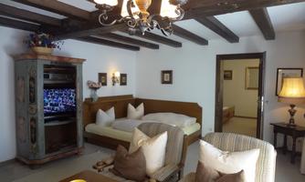 A cozy living room with a wooden ceiling and modern furniture. There is a TV, a large bed, and an inviting seating area with cushions.
