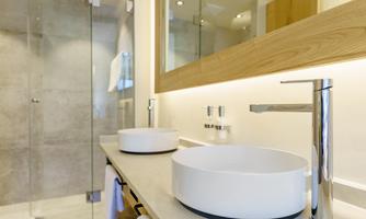 A modern bathroom with two round sinks and a large shower. The walls are bright with wood and glass elements.