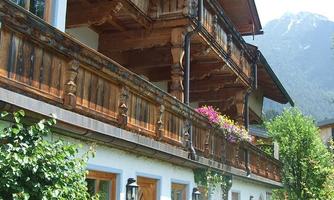 A traditional multi-story wooden house with a balcony and beautiful flowers. Surrounded by lush greenery and mountains in the background.