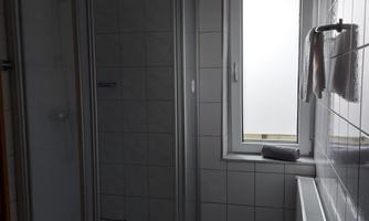 A bathroom with a shower cabin and a window. The tiles are light and the room appears clean and inviting.