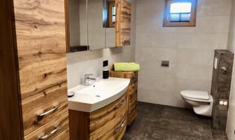 A modern bathroom with wooden cutting cabinets and a sink. There is also a toilet and daylight streaming in through a small window.