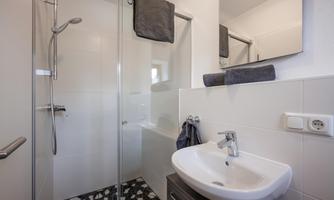 A modern bathroom with a glass shower and a sink. The floor is designed with stylish tiles in black and white.
