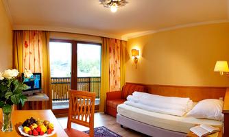 A cozy room with a balcony and large windows. There is a sofa, a table with a fruit bowl, and fresh flowers.
