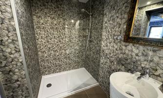 A modern bathroom with a glass shower and an elegant sink. The walls are designed with a striking stone pattern.