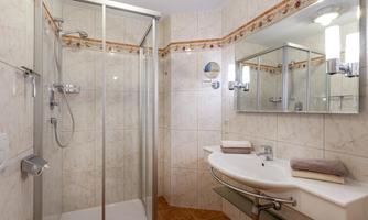 A modern bathroom with a shower cubicle and a sink. The walls are brightly tiled and there are large mirrors.