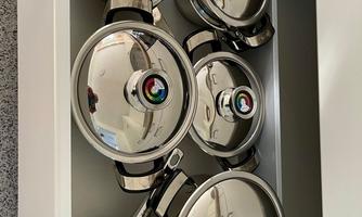 A kitchen drawer with five stainless steel pots and their matching lids. The pots are clean and neatly arranged.
