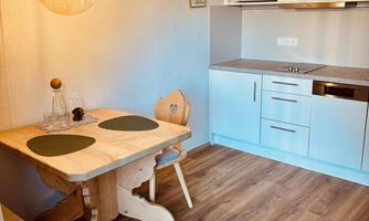 A cozy kitchen with a wooden dining table and two chairs. The modern amenities include a stove, a refrigerator, and a microwave.