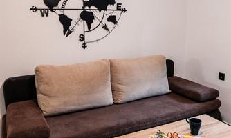 A cozy living room with a brown sofa and a wooden table. On the table, there is a fruit plate, and on the wall, there is a wall clock in the shape of a world map.