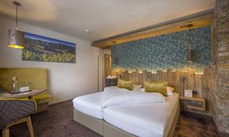 A cozy hotel room with a large double bed and modern decor. The furnishings include a seating area and a stylish wall design.