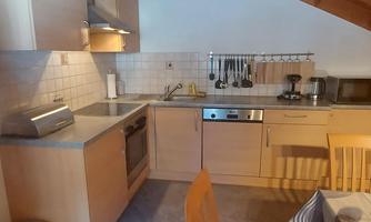A cozy kitchen with wooden shelves and modern appliances. The room has an inviting atmosphere with a table and chairs.