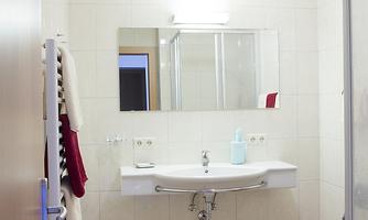 A modern bathroom with a sink, a mirror, and a shower. The walls are light-tiled and the floor is made of marble.