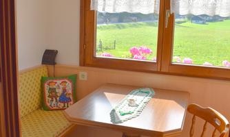 A cozy dining area with a wooden table and chairs. The window offers a view of a green garden with flowers.