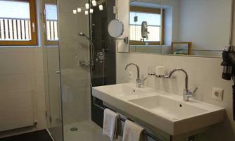 A modern bathroom with a glass shower and two sinks. White walls and wooden windows create a bright and inviting atmosphere.