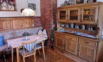 A cozy dining area with wooden paneling and a charming seating corner. The wooden table is lovingly set, and a china cabinet with decorations stands next to it.