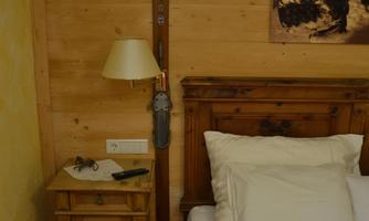 A cozy bedroom with wooden paneling and a bed. On the nightstand are a lamp and some personal items.