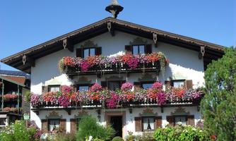 A beautiful house with balcony flowers in bright colors. The garden is lush and green, creating an inviting atmosphere.