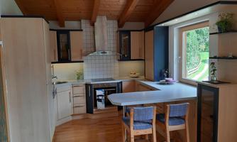 A modern kitchen with wooden ceilings and light cabinets. A table with chairs provides space for eating or for conversations.