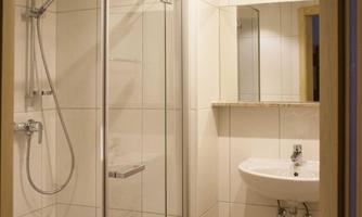 A modern bathroom with a shower niche and a sink.  
Walls are brightly tiled and the lighting is pleasant.