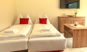 A cozy bedroom with two single beds and red decorative cushions. The room contains a wooden table and a television on the wall.