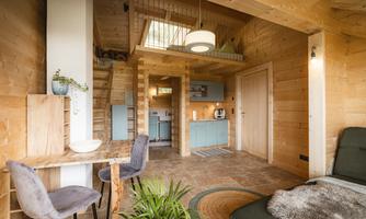 A cozy wooden house with an open living area. The decor is modern and friendly, featuring a dining area and a small kitchen.