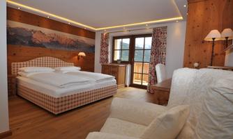 A bright and cozy bedroom with wooden paneling and a large window. The room is furnished with a double bed, an armchair, and a desk.