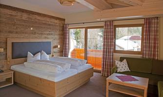 A cozy room with a large wooden bed and a sofa corner. Large windows offer a view of the outdoor terrace.