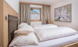 A cozy bedroom with large pillows and a lovely picture on the wall. The windows let in daylight and offer a view of nature.