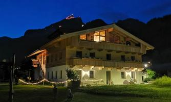 A stylish building with a balcony, illuminated at night. Mountains are visible in the background.