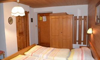 A cozy bedroom with two beds and colorful bedding. There is a wooden wardrobe and a warm, inviting atmosphere.