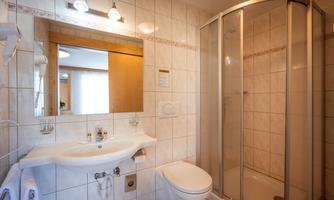 A modern bathroom with a shower, a sink, and a toilet. The walls are tiled and there is mirror lighting.