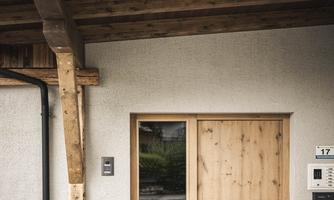 A modern entrance door made of wood with a wooden overhang. In front of the door, there are flowers in pots.