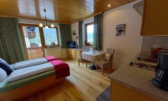 A cozy room with two beds, a table, and chairs. Large windows offer a view of the landscape and plenty of daylight.