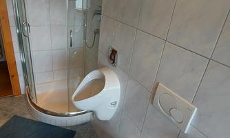 A modern bathroom with a shower and a toilet. The walls are tiled and there is a small rug.