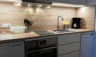 A modern kitchen with wooden details and a clear work surface. Essential kitchen appliances are visible, including a kettle and a coffee machine.