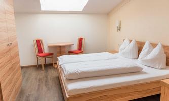 A simple bedroom with a double bed and two red chairs. Large windows provide plenty of natural light and an inviting atmosphere.