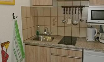 A small kitchen with wooden cabinets and a modern kitchen layout. On the countertop, kitchen utensils and a kettle are visible.