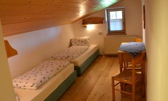 A bright, cozy room with two single beds and a wooden floor. A table and chairs complete the furnishings.
