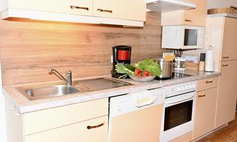 A modern kitchen with light cabinets and a stone countertop. Fresh vegetables and fruit are in a bowl on the table.