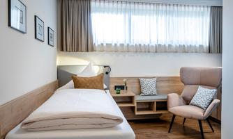 A modern room with a single bed and a cozy armchair. Large windows provide plenty of daylight and a pleasant atmosphere.