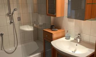 A modern bathroom with a bathtub and shower. The walls are tiled and the room has wooden cabinets for storage.