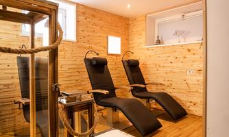 A cozy wellness area with two loungers and wooden paneling. In the foreground, there is a decorative lantern and candles.