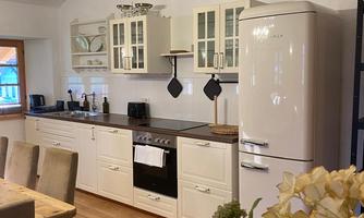 A modern kitchen with white cabinets and a retro-style refrigerator. The wooden floor and the flowers in the foreground add coziness to the atmosphere.