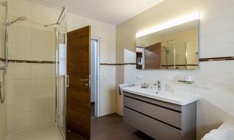 A modern bathroom with a shower and a large mirror. The bright tiles and the wooden cabinet create a pleasant atmosphere.
