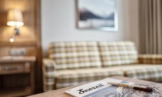 A cozy living room with a checkered sofa and warm wood. On a table lies a magazine titled "Seeziel" and a pen.