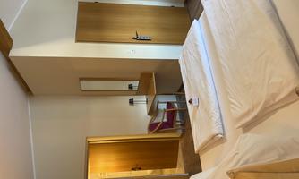 A simple and modern bedroom with two single beds. The room features a table, a chair, and a mirror.