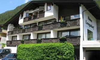 A cozy residence with balconies and green plants. In the background, mountains and blue sky can be seen.